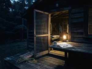 En lägerledarstuga i mörkret, med en fotogenlampa och en uppslagen pärm på verandabordet och ett rep på golvet